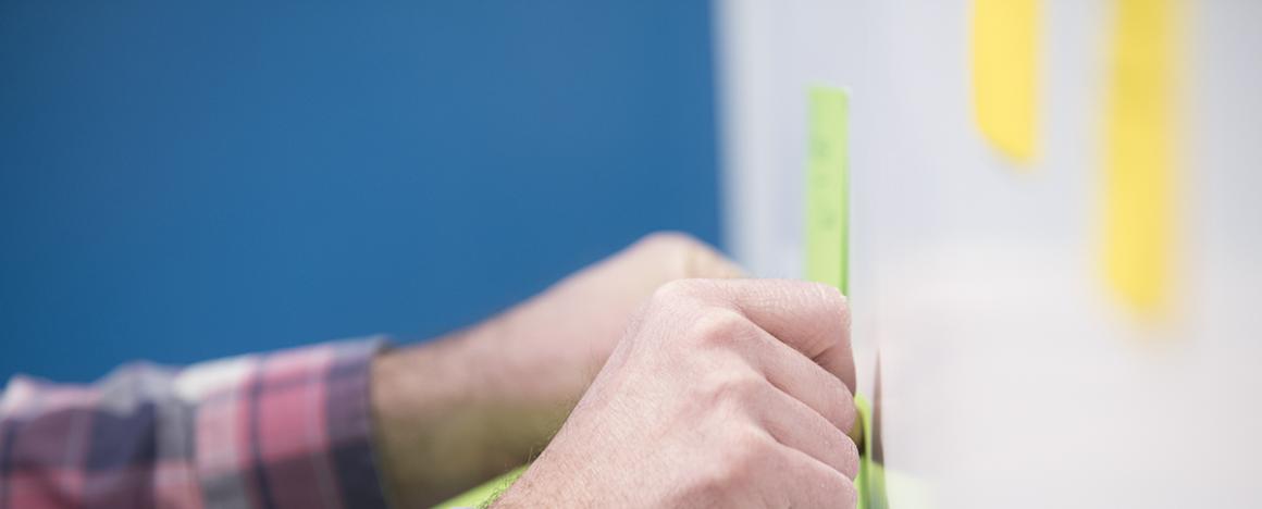 Hands placing sticky note on whiteboard