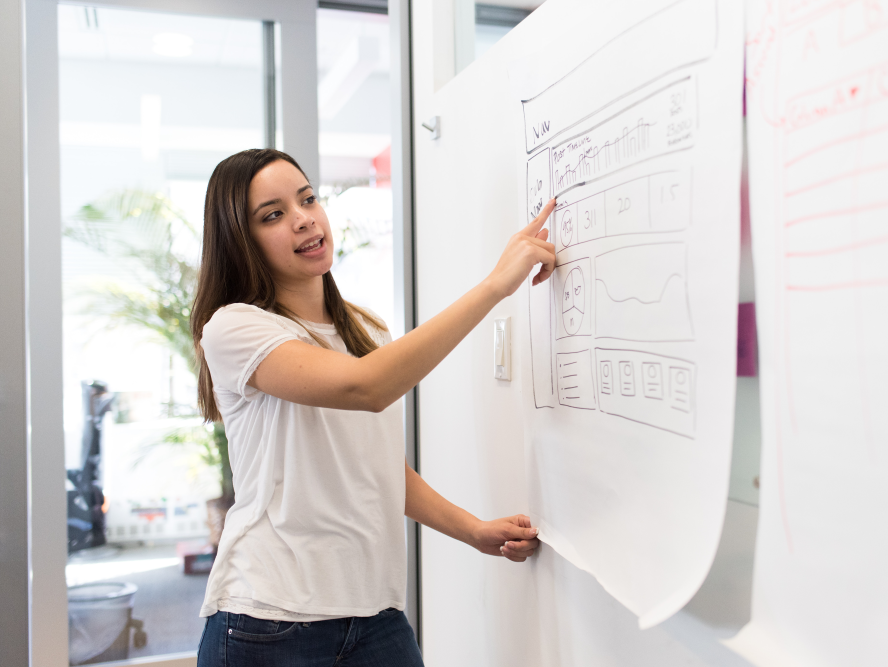 Woman pointing to engineering management data on whiteboard
