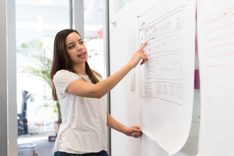 Woman pointing to engineering management data on whiteboard